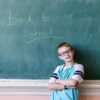 Jonge scholier voor schoolbord met daarop de tekst 'Back to school'.